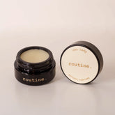 Routine Cat Lady botanic perfume balm - open black glass jar showing cream-coloured solid perfume with detached lid displaying product name - natural moisturizing fragrance balm